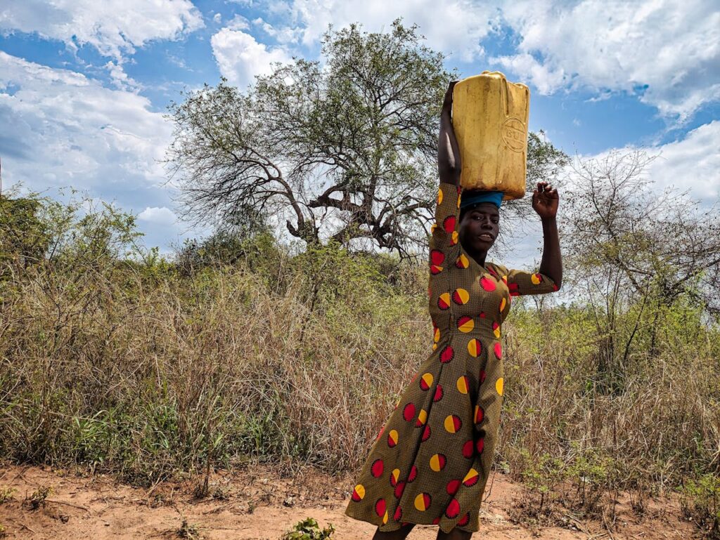 Woman in Patterned Dress Carrying Container on Head